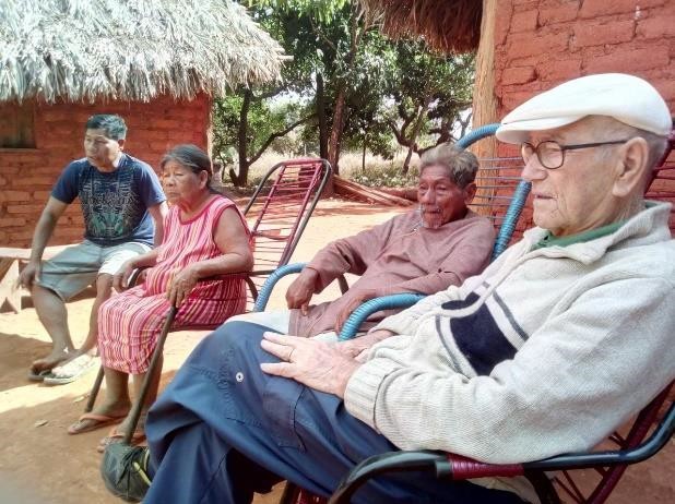 Rinaldo sentado numa cadeira em frente a anciãos indígenas