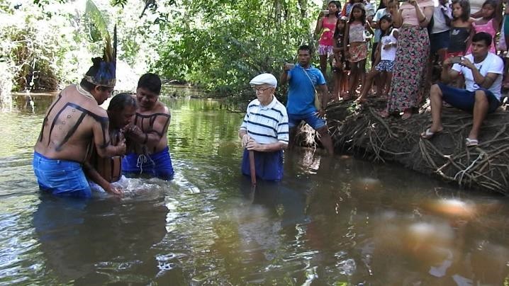 Indígenas batizam um parente enquanto Rinaldo e outros indígenas observam